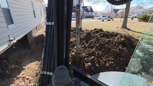 Foundation stabilization in progress showing excavation, pier driving, and hydraulic lifting at a residential home