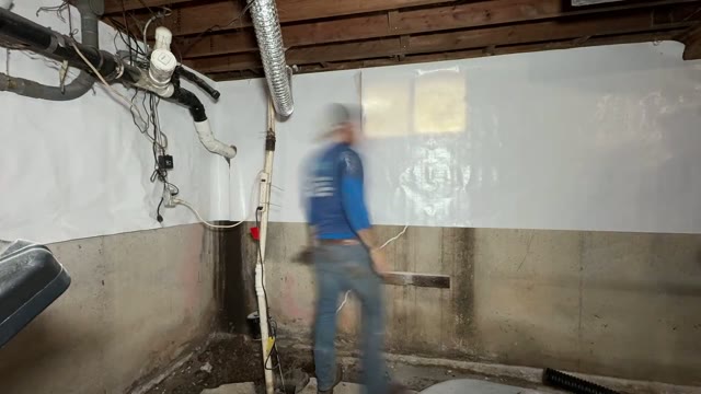 JLB crew continuing vapor barrier installation along a basement foundation wall during a waterproofing project